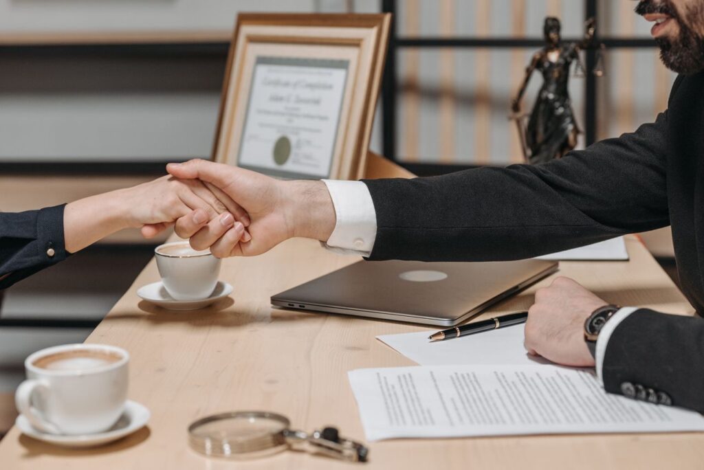 Two business professionals shaking hands over a signed contract at an office meeting table