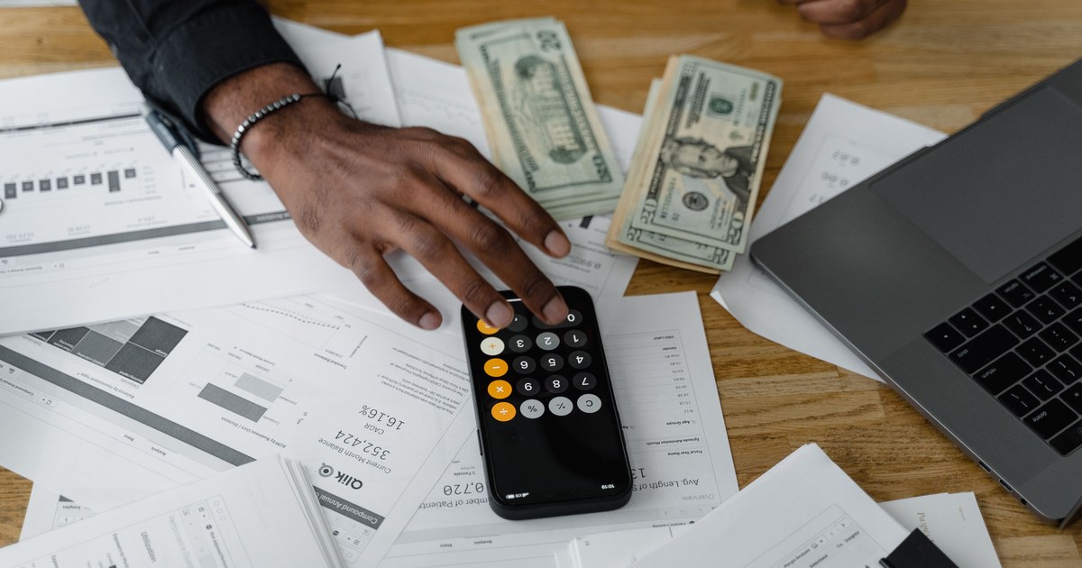 Hand using a calculator over financial documents and a laptop, representing production budget review